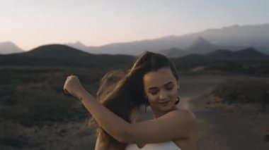 Güzel, uzun saçlı kız dans ediyor ve poz veriyor dağların arka planında ve muhteşem doğada. Adada gün batımı, atmosferik tonlama. Tender video, doğayla bütünlük, mutluluk.