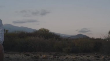 Sırt çantalı bir gezgin dağlarda beyaz bir adada bir kaktüsün yanında oturuyor ve ona dokunuyor..
