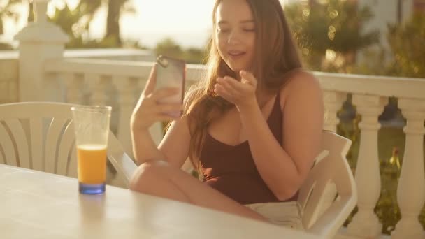 Lány Teraszon Naplemente Hátterében Nyári Hajnalban Egy Gyümölcslevet Iszik Telefonon — Stock videók