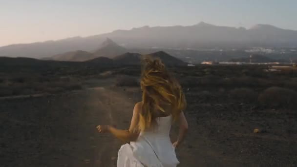 白い長いドレスを着た女の子が旅に走り 自由を楽しんでいます 長い夕日に対して山の中で髪の美しさ 島の美しさ — ストック動画