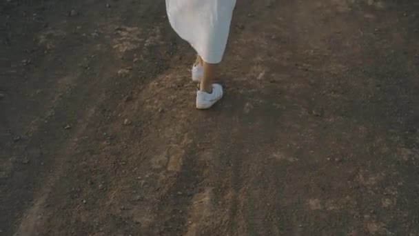 少女は日没時に夏の島を歩く 美しさと長い白いドレスの女の子の足の山 石の上を歩く 大気ビデオ — ストック動画