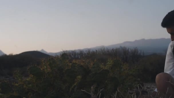 白い島の山の中にリュックを持つ旅行者は サボテンの近くの山の中に座って それに触れます — ストック動画