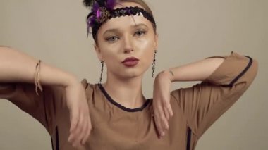 90 'ların tarzında bir kız, Chicago tarzı. Şapka, kafasında dekoratif tüy olan saç bandı. İnanılmaz mücevherler, elmaslı uzun küpeler, coquette. Gülümsüyor ve gülüyor. Gülümse, dans et.