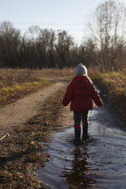 Su birikintisinde köpüklerle yürüyen bir çocuk.