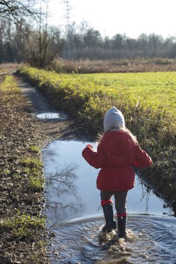 Kırmızı ceketli ve çizgili su birikintisinde yürüyen bir çocuk..