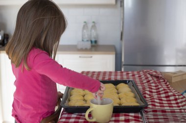 Mutfakta yumurtalı çörekleri pişirmeden önce yumurta banyosuyla parlatan bir kız çocuğu. Anaokulu öğrencileri için kilitleme etkinliği fikri.