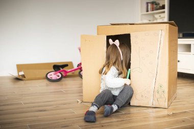 Yeni bir eve taşınırken karton bir oyun evinde oturan küçük kız çocuğu. Anaokulu öğrencileri için kilitleme etkinliği fikri.