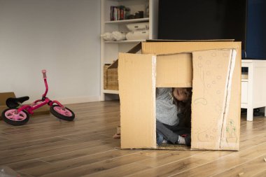 Yeni bir eve taşınırken karton bir oyun evinde oynayan küçük bir kız çocuğu. Anaokulu öğrencileri için kilitleme etkinliği fikri.
