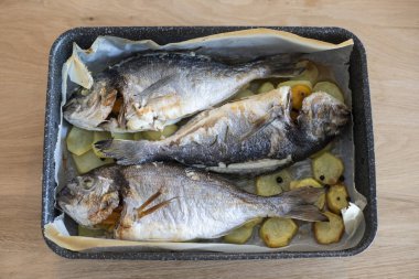 Tahta bir zeminde, dilimlenmiş patatesle pişirilmiş ve süslenmiş bir tavada üç deniz çamı..
