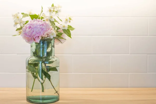 Flowers bouquet with peony (paeonia) and mock-orange (philadelphus), in a blue glass vase with white tiles backsplash in the background. Spring wallpaper with copy space.