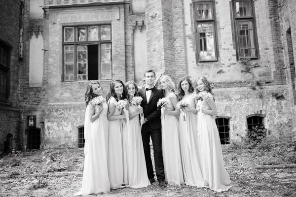 groom posing with  bridesmaids dressed in long elegant dresses