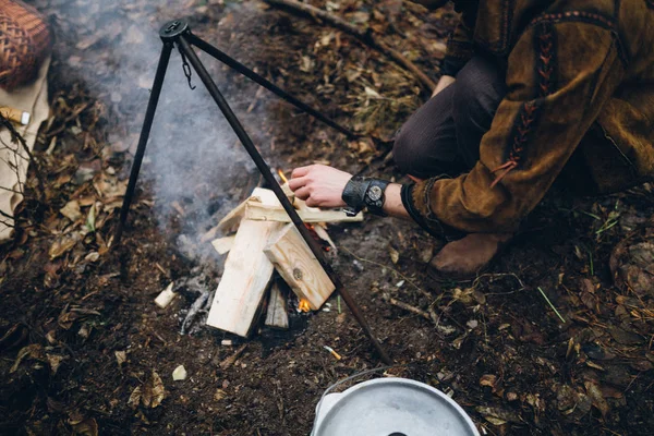 森の中で夕食の火に燃料を供給する男 — ストック写真