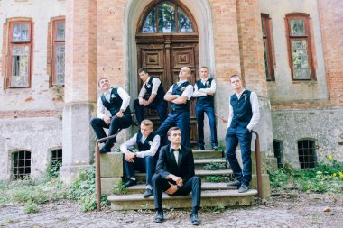 young groom with  groomsmen  posing near old building  clipart