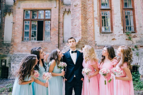 groom posing with  bridesmaids dressed in long elegant dresses