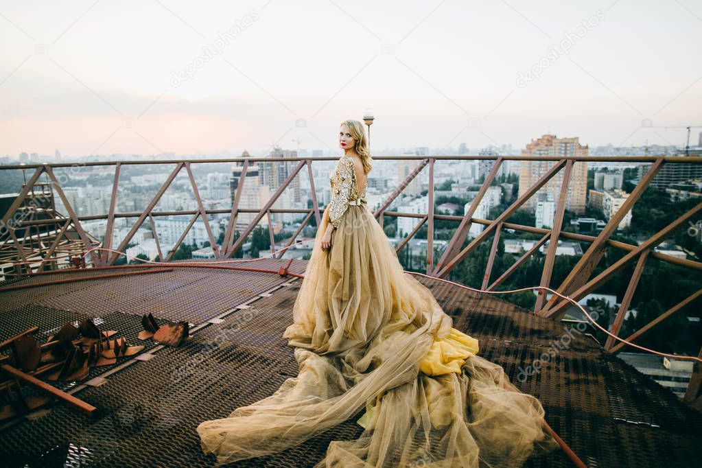 Elegant woman  wearing golden  dress and posing  on the roof