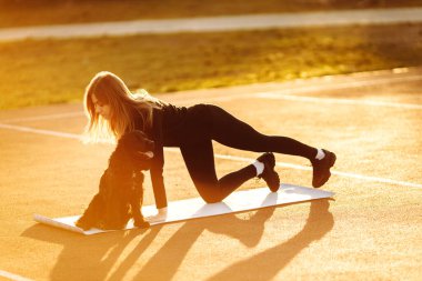 Genç, formda bir kadın köpeğiyle parkta egzersiz yapıyor. 