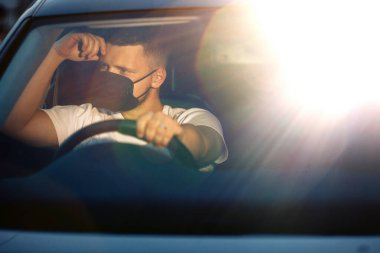 Arabada maske takan genç bir adam.