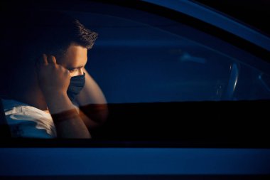 Arabada maske takan genç bir adam.