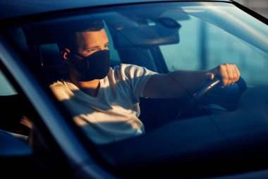 Arabada maske takan genç bir adam.