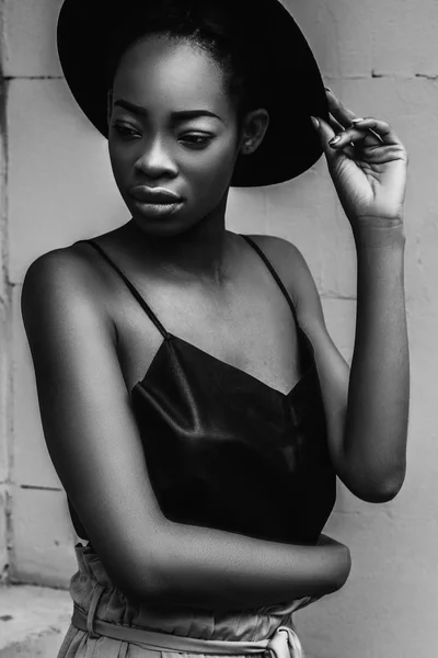 Portrait of African female model in fashion hat posing outdoor on grey background.