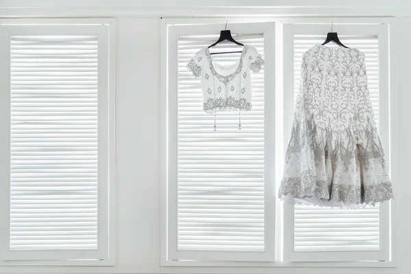 The indian wedding dress, saree and blouse hanging with the white windows with light in background.