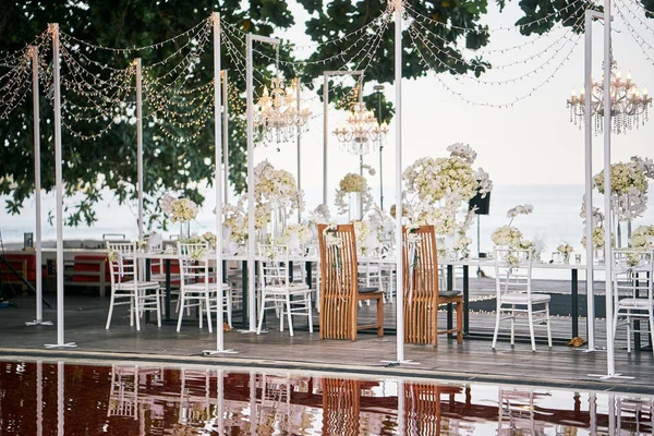 The bride and the groom seat from behind at the reception dinner table preparation with white roses, white orchids decoration