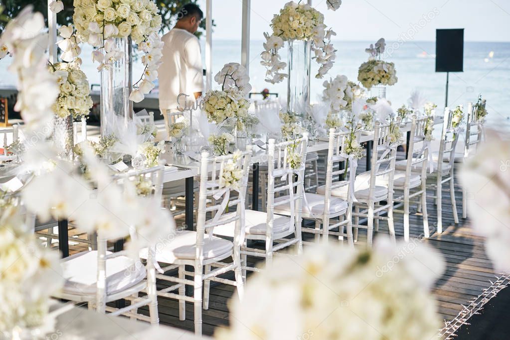 The wedding venue for reception dinner table decorated with white orchids, white roses, flowers, floral, white and clean theme on the Beach