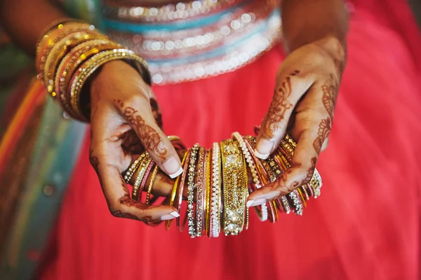 A mão com mehndi de noiva indiana segurando um monte de pulseiras glitter (pulseira) com fundo lenha vermelho, close-up — Fotografia de Stock