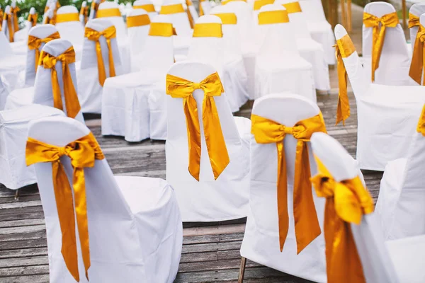 Um grupo de cadeiras de elastano branco cobrir com faixa de organza ouro para arranjo local de casamento na praia — Fotografia de Stock