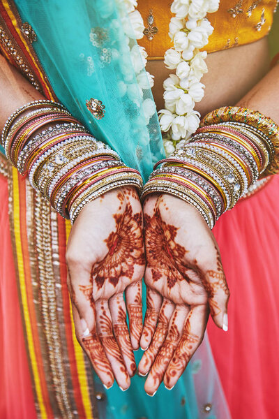 The close-up shot of Indian bride with beautiful saree in yellow blouse and red legenha showing hand with mehndi painted (henna) with a lot of glitter bracelets (bangle) on her wrist