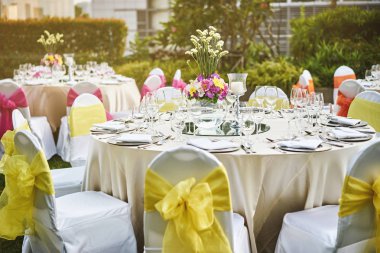 Resepsiyon akşam yemeği sofra ile boş bardak su, şarap ve çiçek dekorasyonu ile dinnerwear ve beyaz kumaş kapak sandalye sarı kanat ile düğün