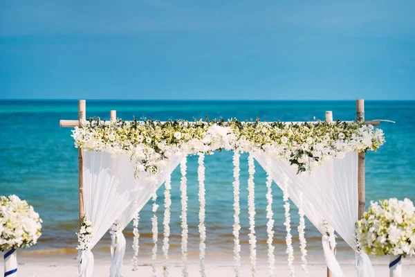 The beautiful wedding venue setting with white and green flowers, floral decoration on bamboo arch with panoramic ocean view in background