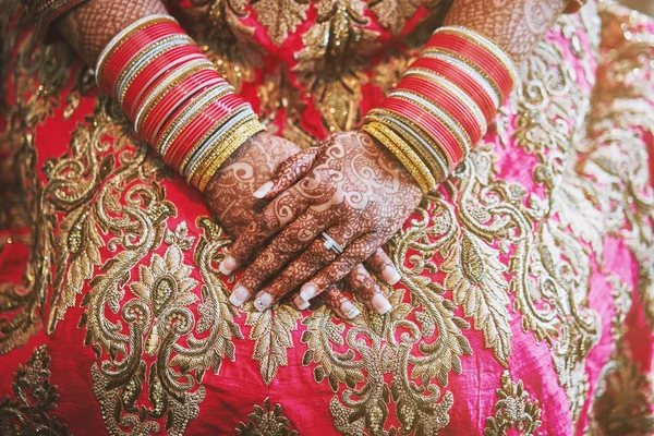 The close-up shot of Indian bride with beautiful pink saree showing mehndi (henna) hand with a lot of glitter bracelets (bangles) on her wrist