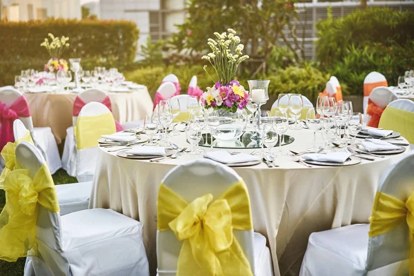 Resepsiyon akşam yemeği sofra ile boş bardak su, şarap ve çiçek dekorasyonu ile dinnerwear ve beyaz kumaş kapak sandalye sarı kanat ile düğün