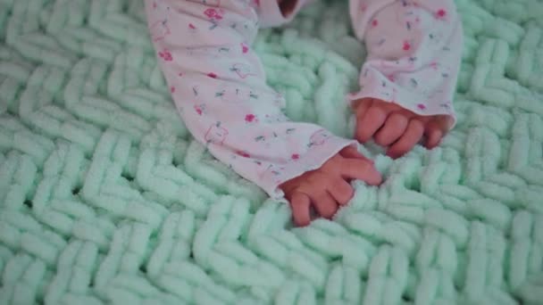 Az újszülött megérinti a plédet. Egy kisbaba keze mászik egy zöld kötött takarón. Közelkép.. — Stock videók