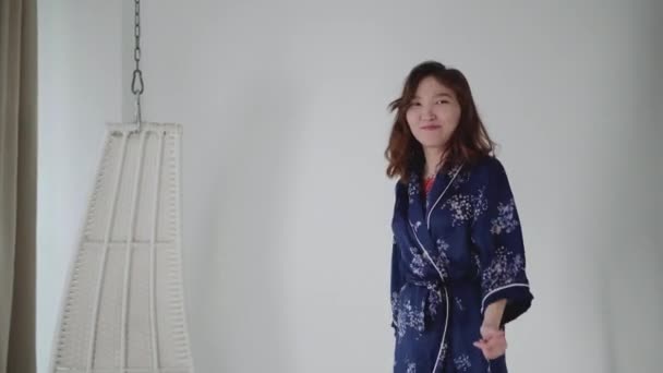 Jeune fille asiatique heureuse posant dans un studio lumineux en pyjama bleu . — Video