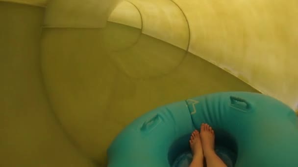 Descente d'un toboggan aquatique jaune dans un parc aquatique sur un anneau en caoutchouc bleu. Vue à la première personne des pieds d'une jeune fille. Traitements de l'eau - plaisir à la station . — Video