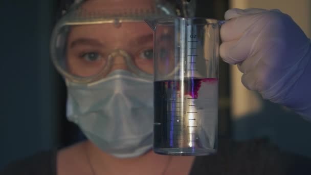 水で測定ガラスを持っている若い医師の少女の肖像画 紫色の過マンガン酸カリウムを美しく水に注ぐ 成分の混合 コロナウイルスワクチンの発明 — ストック動画