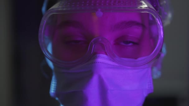 若い女の子の医者の閉鎖肖像画 医療用マスク キャップは科学者の頭を保護します 紫色の照明のあるオフィスでコロナウイルスワクチンを作成する — ストック動画