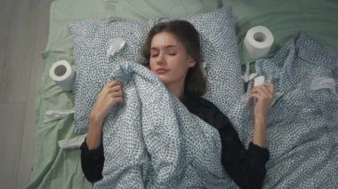 Hasta kız yorganın altında yatıp burnunu siliyor. Mendil gibi koronavirüsteki tuvalet kağıdı salgını. Coronavirus koruması. Carntin zamanında evde tedavi.