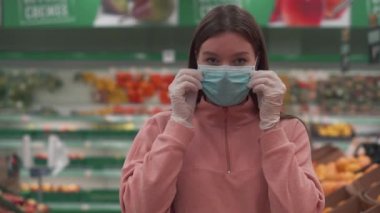 Genç ve güzel bir kız bir mağazada tıbbi maske takıyor. Alışveriş merkezi Coronavirus 'a boşaldı. Enfeksiyonun yayılması ve bulaşmasına karşı koruyucu eldivenler.