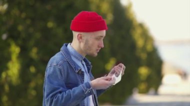 Kırmızı şapkalı genç adam koruyucu maske takıyor.