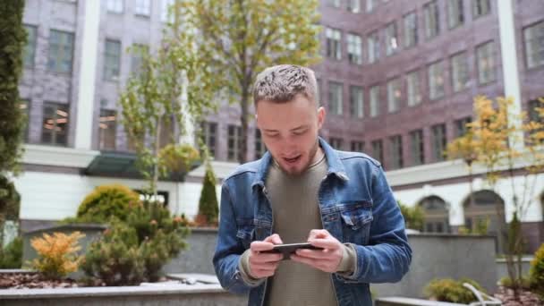 Jonge Man Speelt Telefoon Tegen Achtergrond Van Het Kantoor Centrum — Stockvideo