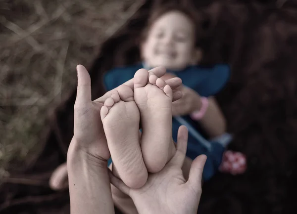 Piccole dita di piccole gambe di bambino in calde mani materne . — Foto Stock