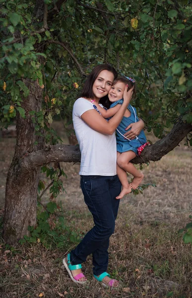 リンゴの庭を散歩している家族 子供を持つ幸せな若い母親 美しいです若いです女性抱擁彼女の笑い娘 — ストック写真