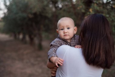 Bebek annemin omzundan dışarı bakıyor. Bebek, kızın kollarındaymış. Açık hava çocuk portresi.