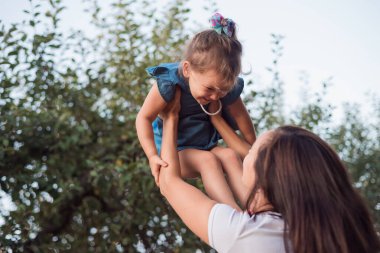 Mutlu gülen çocuk. Bahçede genç bir anne ve kızın aktif oyunu. Mutlu küçük bir kız annenin ellerinde..