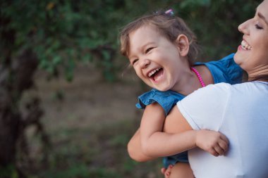Bahçede genç bir anne ve kızın aktif oyunu. Mutlu küçük bir kız annenin ellerinde. Mutlu gülen çocuk.