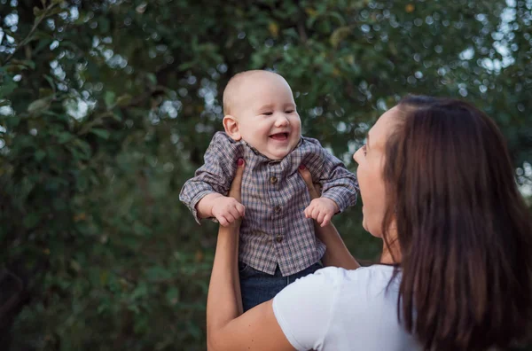 Bebek annenin ellerinde mutlu bir şekilde güler. Çocukla eğlenceli bir oyun. Genç anne ve küçük dişsiz çocuk