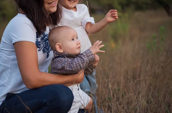お母さんと妹の近くのケージシャツの中のスタイリッシュな美しい赤ちゃん 子供の感情を楽しませる 子供は刃を捕まえる 小さなふっくらしたハンドルのザモル — ストック写真